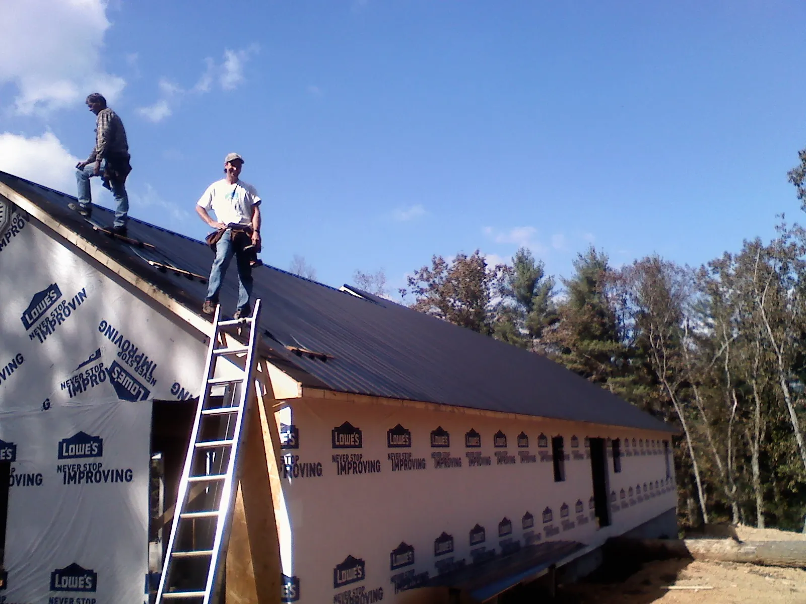Two roofers standing on a long dark metal roof over a wrapped building in Greenville